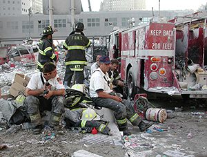A group of firefighters sitting on piles of rubble in the street.