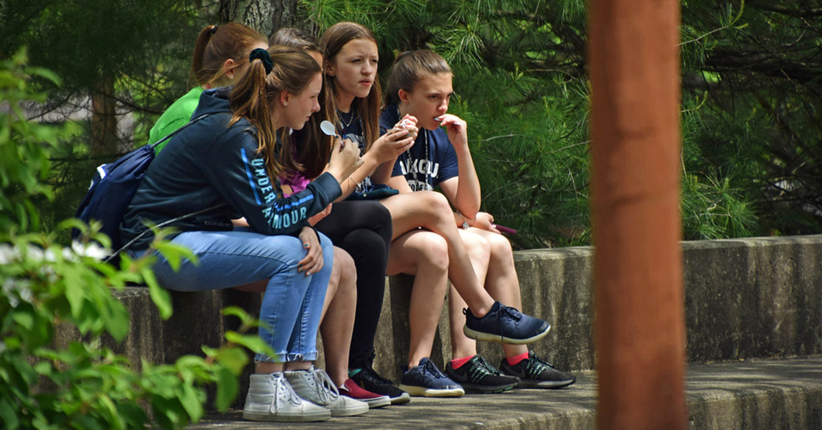 Teenagers sit on a wall eating snacks.