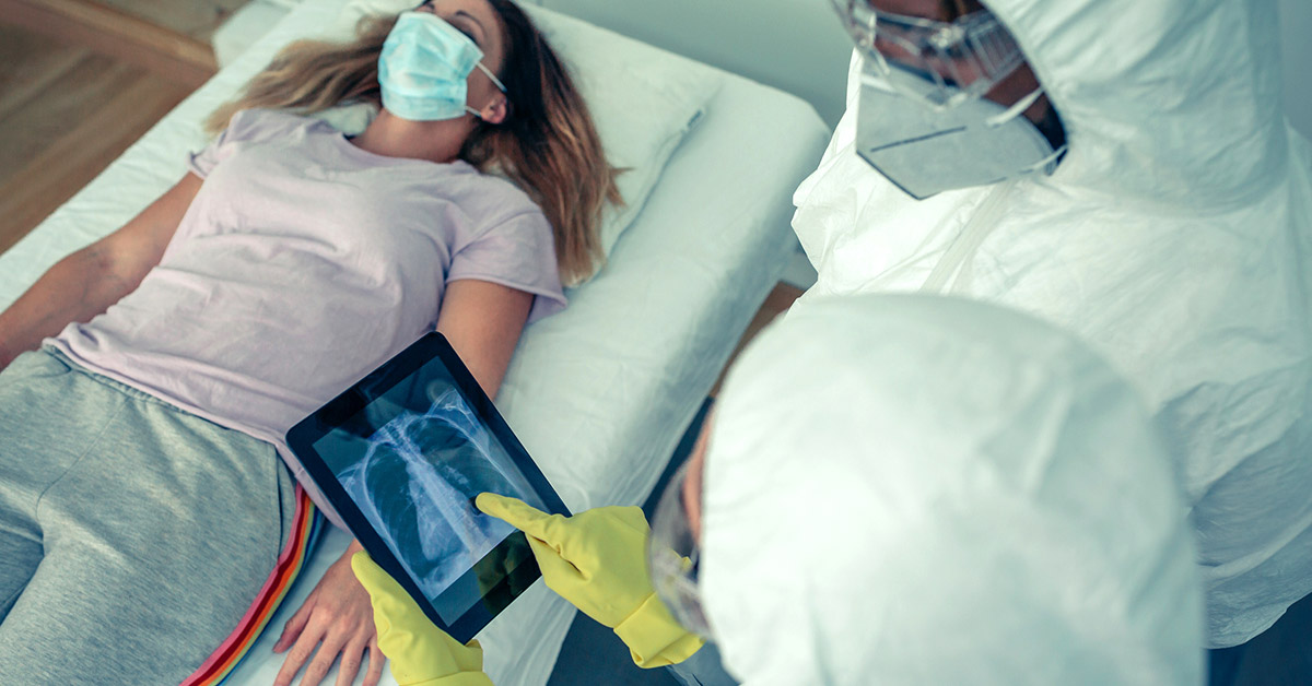 A patient lies on a table as health care staff examine images of her lungs.