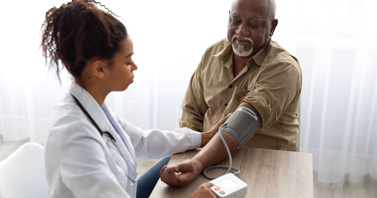 older Black man has his blood pressure checked by female medical worker in white lab coat