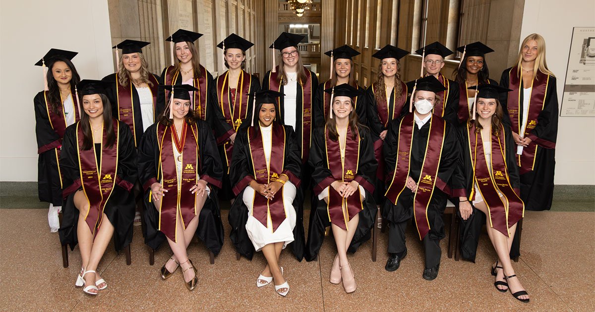 A group of young people wearing graduation robes and mortarboards pose for a formal photo